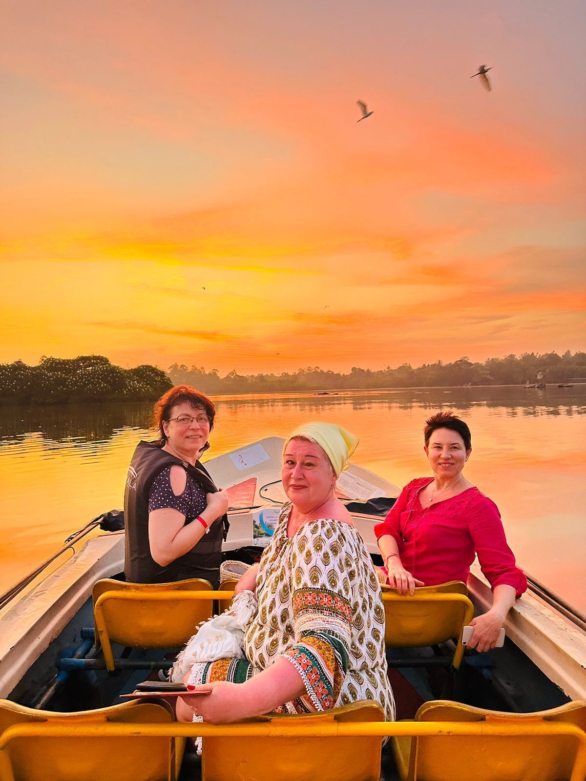 Tres personas en un bote con un atardecer al fondo.