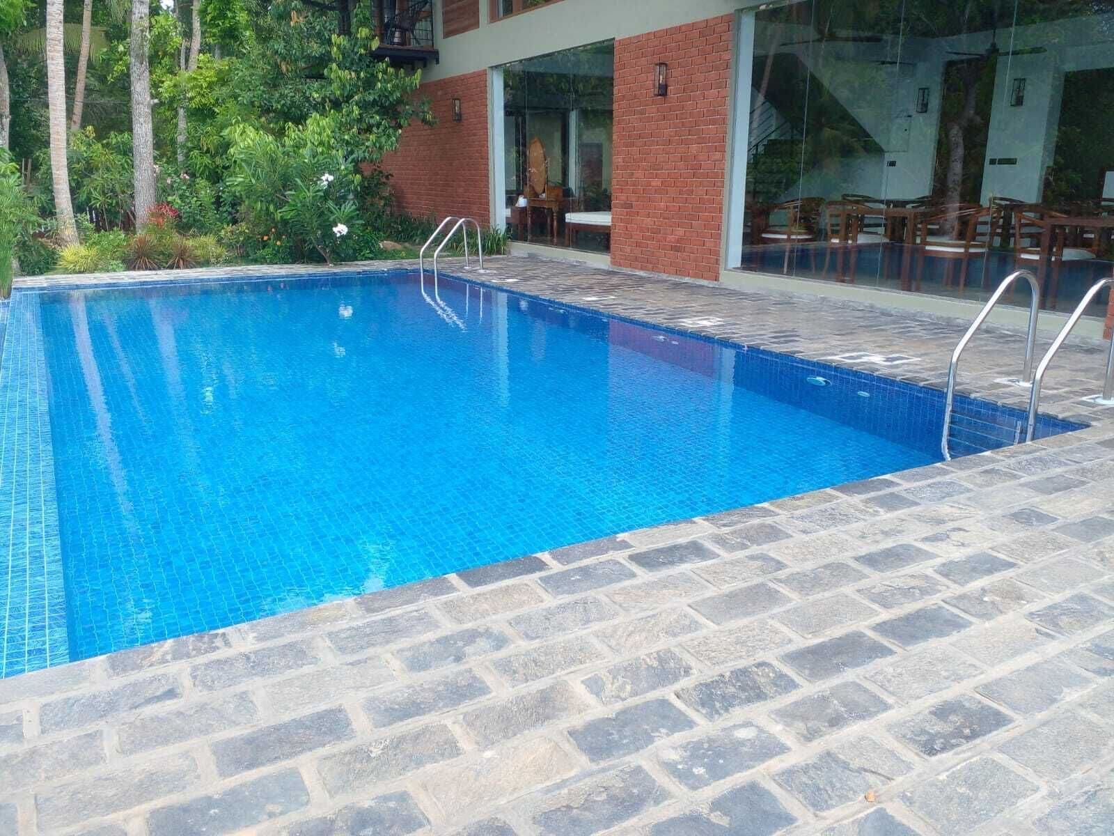 A rectangular swimming pool with clear blue water, surrounded by stone tiles and a brick wall.