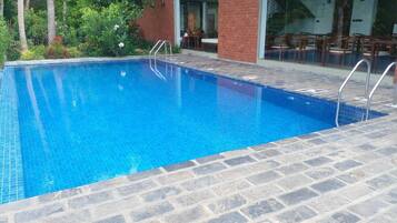 A rectangular swimming pool with clear blue water, surrounded by stone tiles and a brick wall.