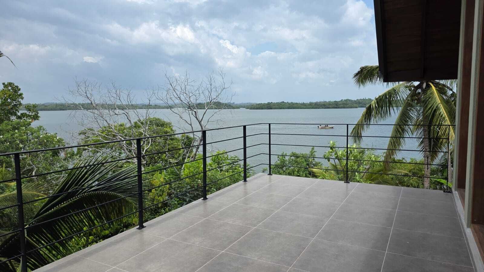 Un balcon offrant une vue sur un lac et sur des terres lointaines, le tout entouré de verdure.