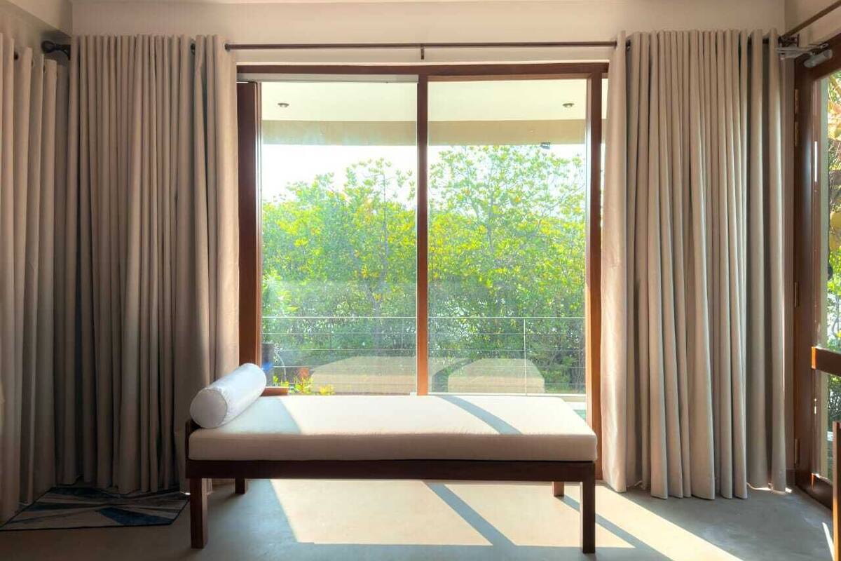 Une chambre à coucher avec un lit, des rideaux et une vue sur la verdure.