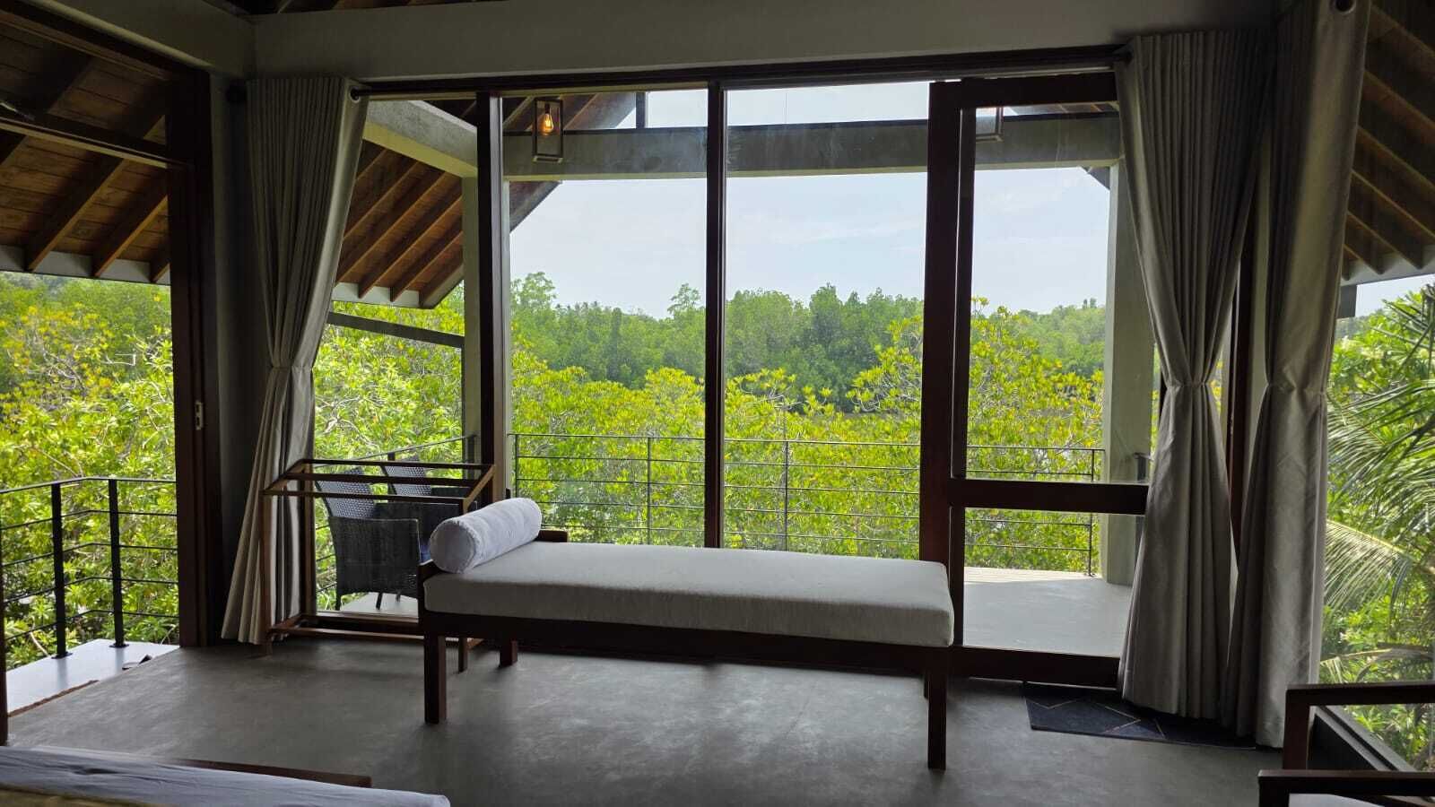A room with a bed, a chair, and a balcony with a view of greenery.