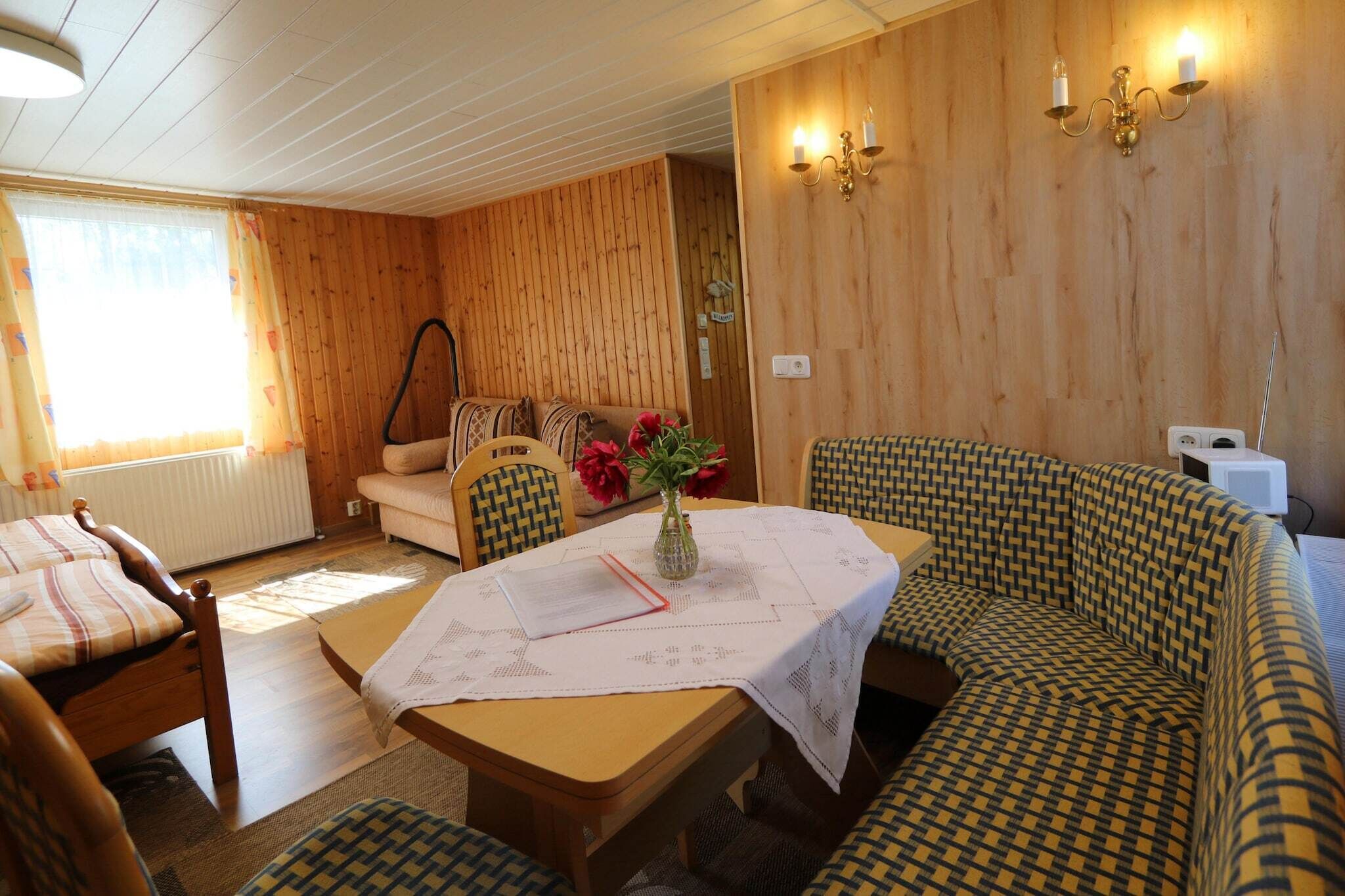 A cozy room with a wooden wall, a sofa, a table with a vase, and a chair.