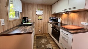 A compact kitchen with wooden cabinets, a coffee maker, an oven, and a window with a curtain. - Fabulous Bungalow in Steffenshagen near Sea (Steffenshagen)