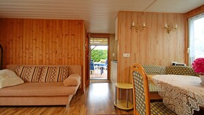 A wooden interior with a sofa, a dining table with a lace tablecloth, and a chair. - Fabulous Bungalow in Steffenshagen near Sea (Steffenshagen)