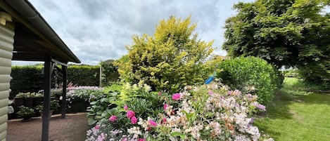 Un jardín con un sendero de ladrillo, un pérgola y diversas plantas en flor.