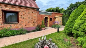 A brick house with a tiled roof, a paved pathway, and a well-maintained garden with various plants and a decorative tree. - Fabulous Bungalow in Steffenshagen near Sea (Steffenshagen)