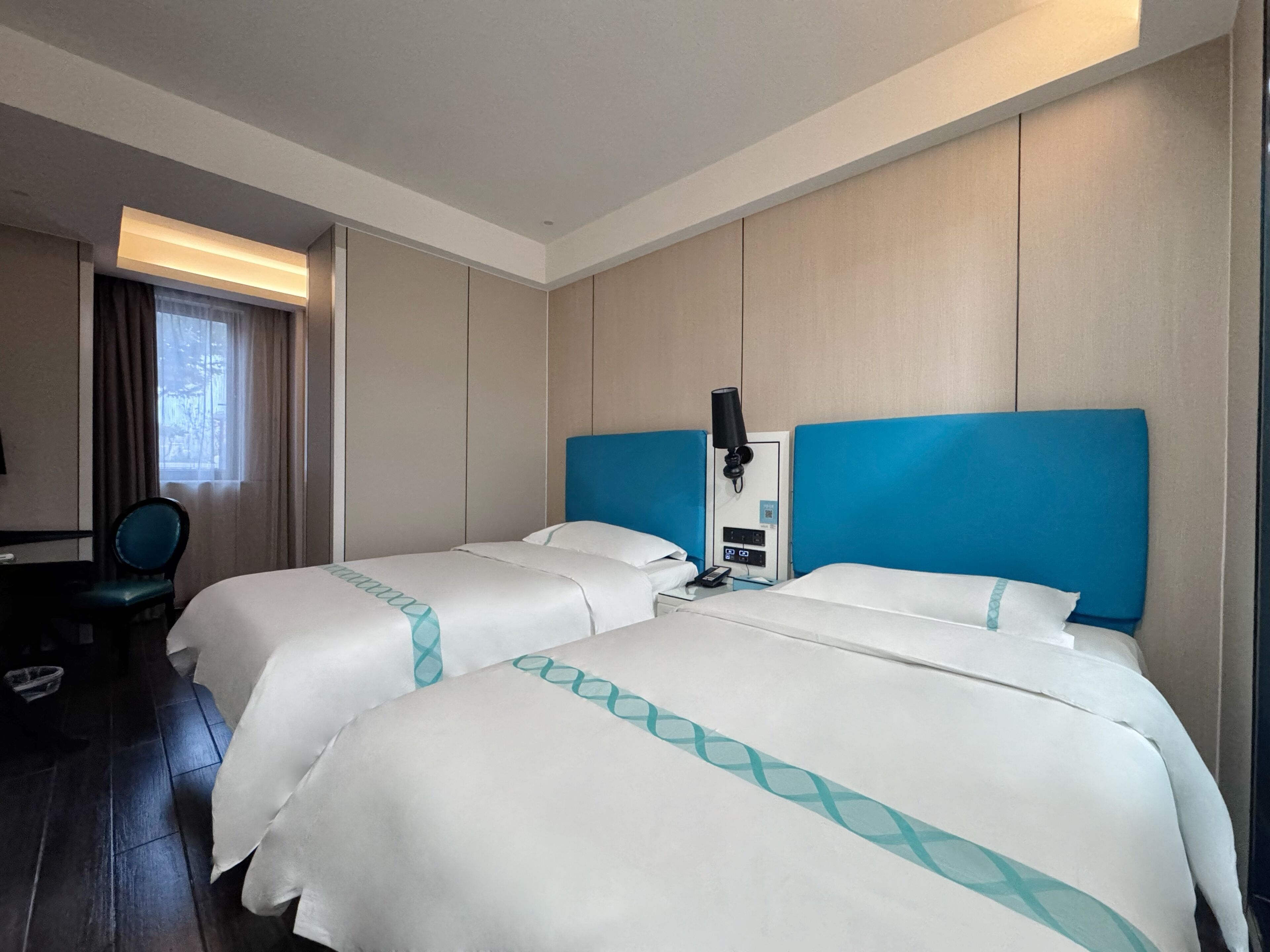 Ett hotellrum med två sängar, ett skrivbord, en stol och ett fönster med gardiner.