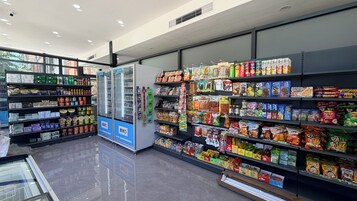 Interior de una tienda de comestibles con estantes llenos de diversos alimentos, un refrigerador y una máquina expendedora.