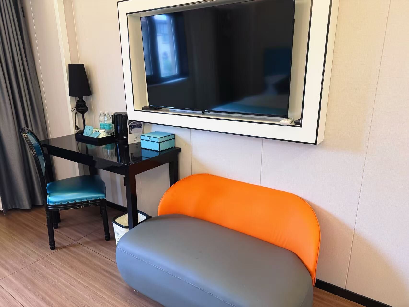 Habitación de hotel con una televisión montada en la pared, un escritorio con una silla y una zona de estar con asientos acolchados.