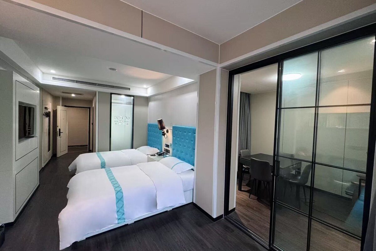 Hotelkamer met twee bedden, een bureau, een stoel, een televisie en een schuifdeur naar een balkon.