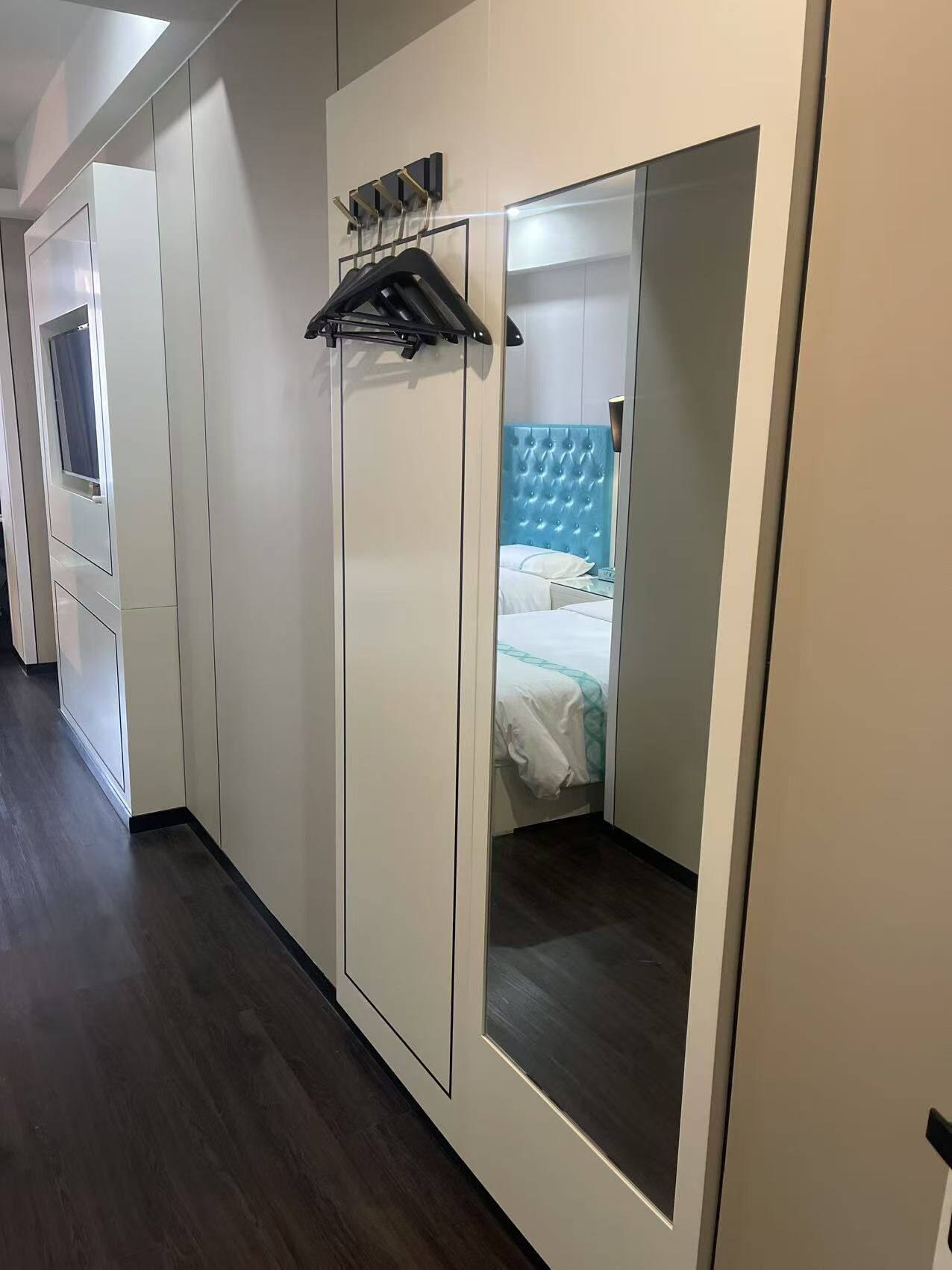 Habitación de hotel con armario, espejo, cama con cabecera azul y perchero.