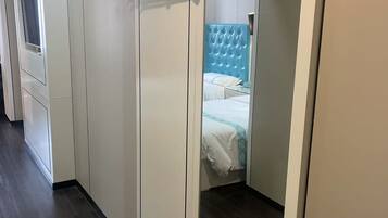 Habitación de hotel con armario, espejo, cama con cabecera azul y perchero.