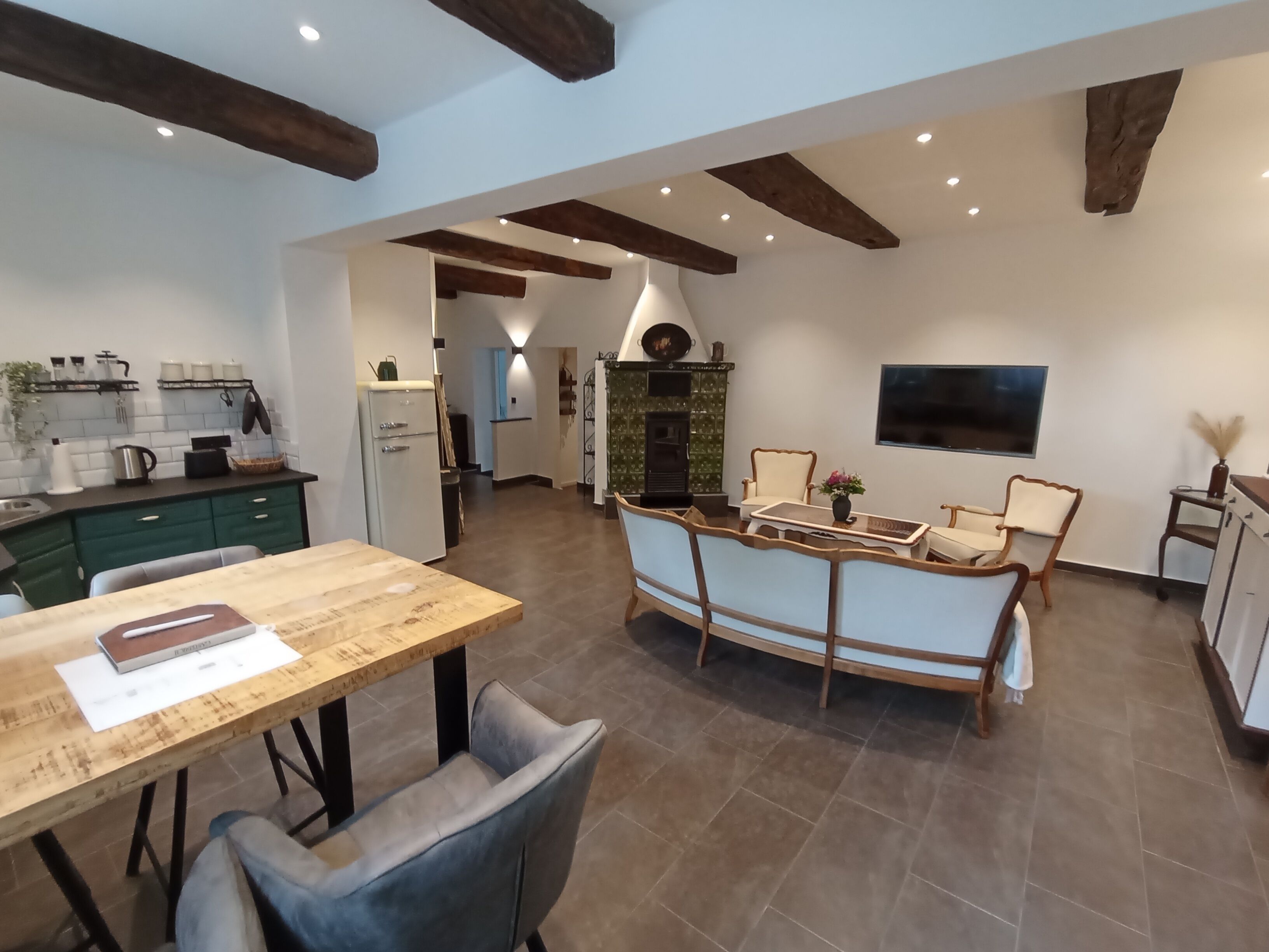 Une cuisine spacieuse équipée d’appareils électroménagers modernes, un coin repas avec une table et des chaises en bois, et un coin salon confortable avec un canapé et des fauteuils.