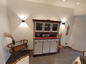 A room with a wooden cabinet with glass doors, a small table, and a chair. - Müllerstube im Müllerhaus (Lübeck)