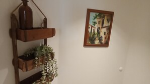 A corner of a room with a wooden shelf holding a vase and plants, and a framed painting on the wall. - Müllerstube im Müllerhaus (Lübeck)