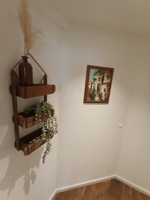 Ein Raumeck mit einem hölzernen Regal, das eine Vase und Pflanzen beherbergt, sowie ein gerahmtes Bild an der Wand.