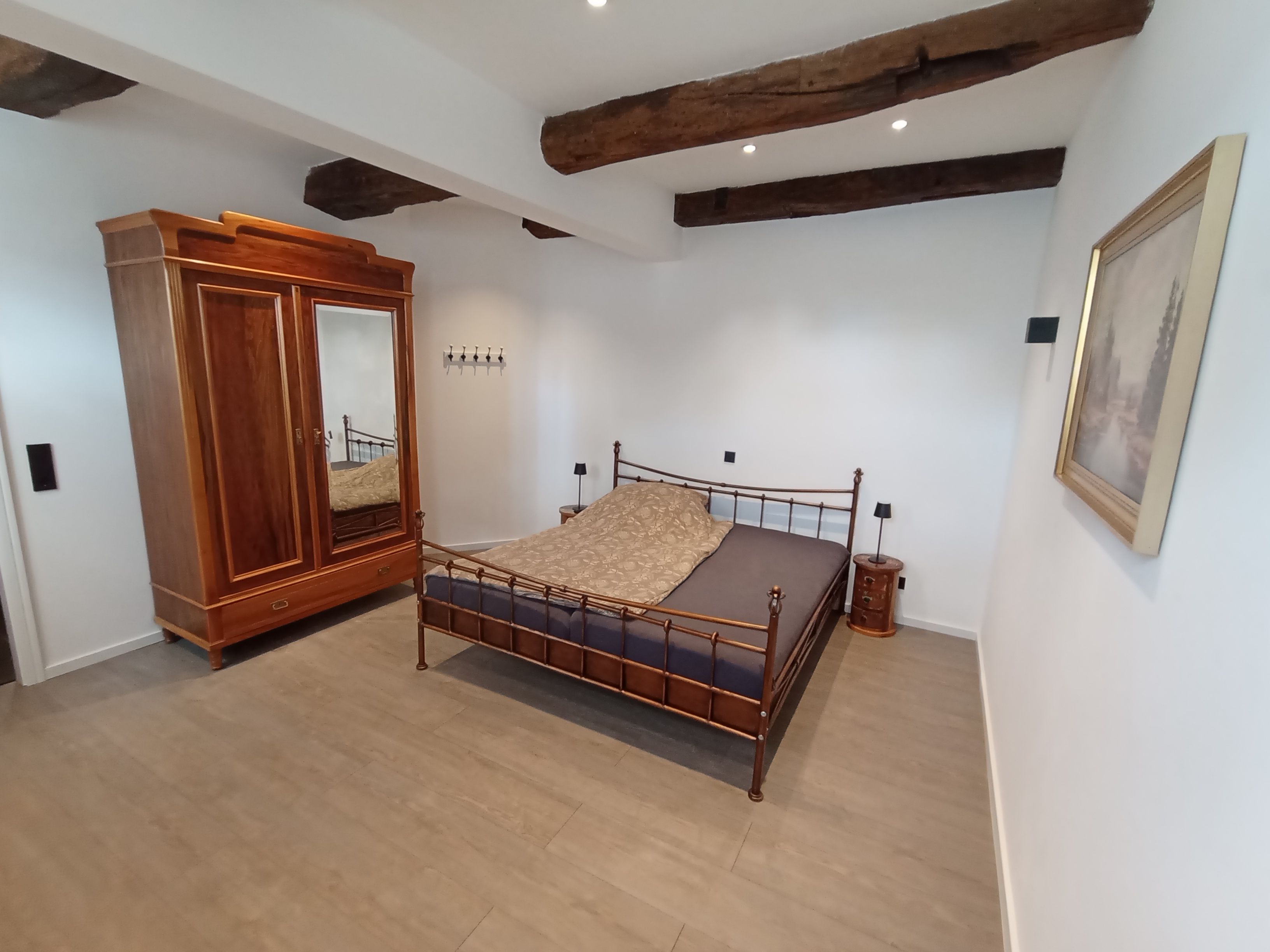 A bedroom with a wooden wardrobe, a bed with a patterned bedspread, and a single bedside table.