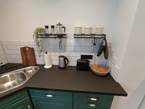 Eine Küche mit Spüle aus Edelstahl, Wasserkocher, Toaster und einer Körbe auf der Arbeitsfläche.