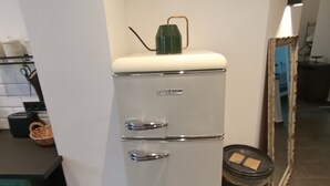 A compact, white refrigerator with a green top, located in a kitchen with a tiled floor and a mirror on the wall. - Müllerstube im Müllerhaus (Lübeck)