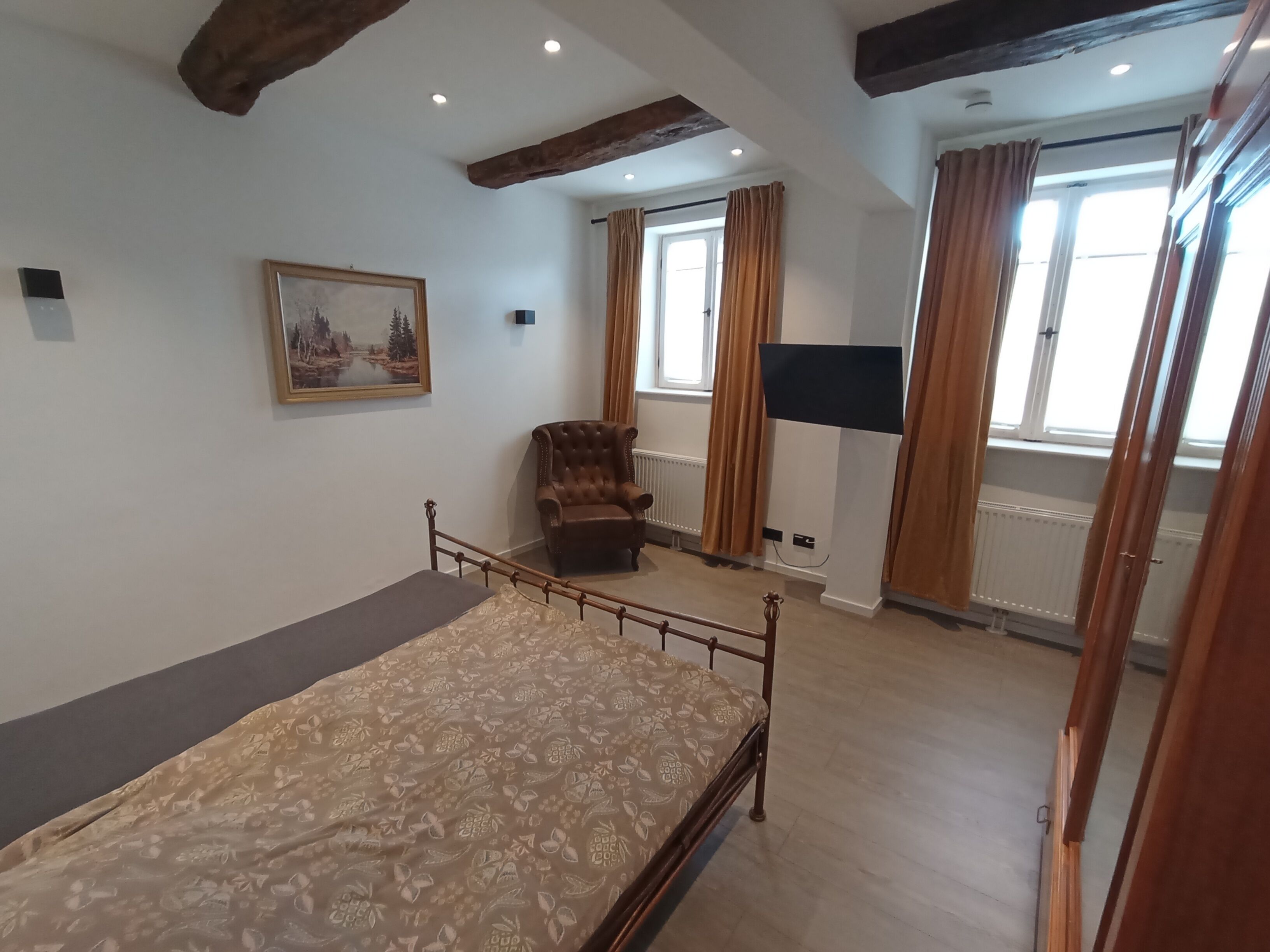 Een slaapkamer met een bed, een stoel, een schilderij, een televisie en een raam met gordijnen.