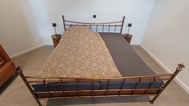 A bed with a patterned bedspread, two bedside tables, and a wooden headboard. - Müllerstube im Müllerhaus (Lübeck)