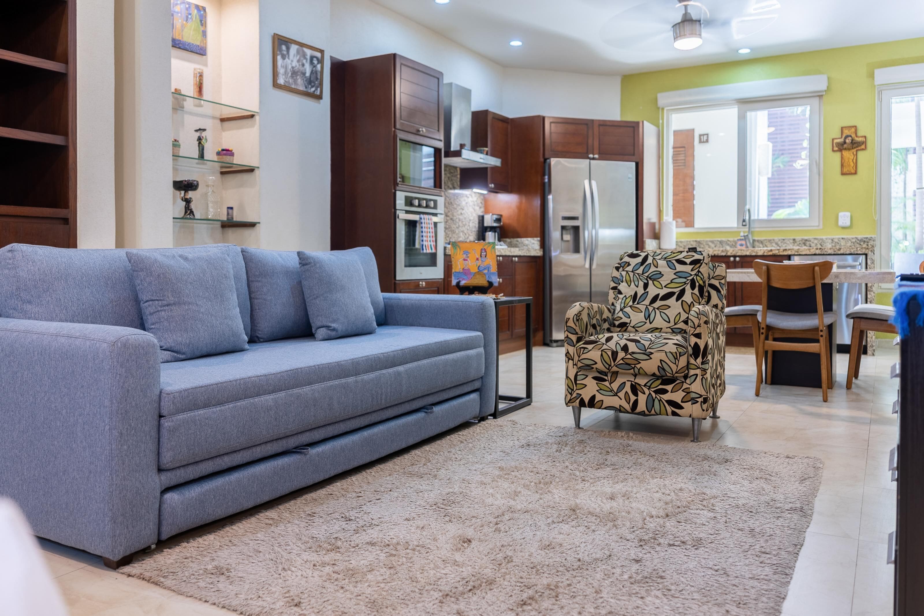 Un salon comprenant un canapé, un fauteuil à motifs et un coin cuisine avec des placards et des appareils électroménagers.