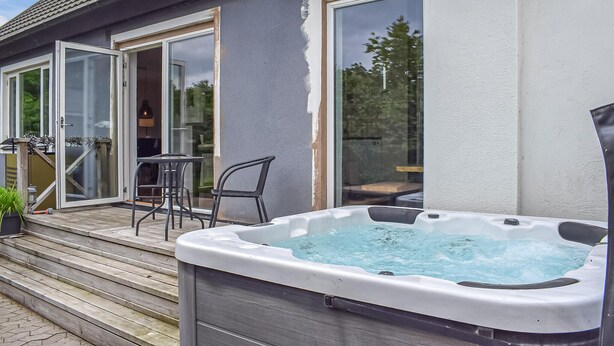 Un bain à remous sur une terrasse en bois, une porte vitrée et un fauteuil.