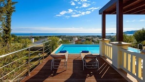 A wooden deck with two lounge chairs overlooking a swimming pool and a scenic view of the sea and distant landscape. - Villa Daphne in Inverness (Rhodes)