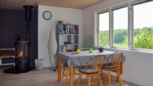 Une pièce avec une cheminée, une bibliothèque, une table à manger avec des chaises et une fenêtre donnant sur un paysage verdoyant.