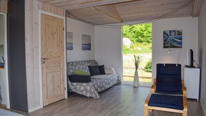 Une pièce avec une porte en bois, un canapé recouvert d’un tissu à motifs, une chaise bleue et une petite table avec une lampe.