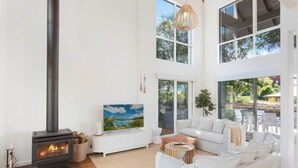 A modern living room with a fireplace, white furniture, and large windows. - Maisie's by Holiday Management Co. (Bega Valley)