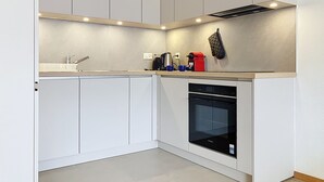 Uma cozinha moderna com armários brancos, forno embutido e cafeteira.