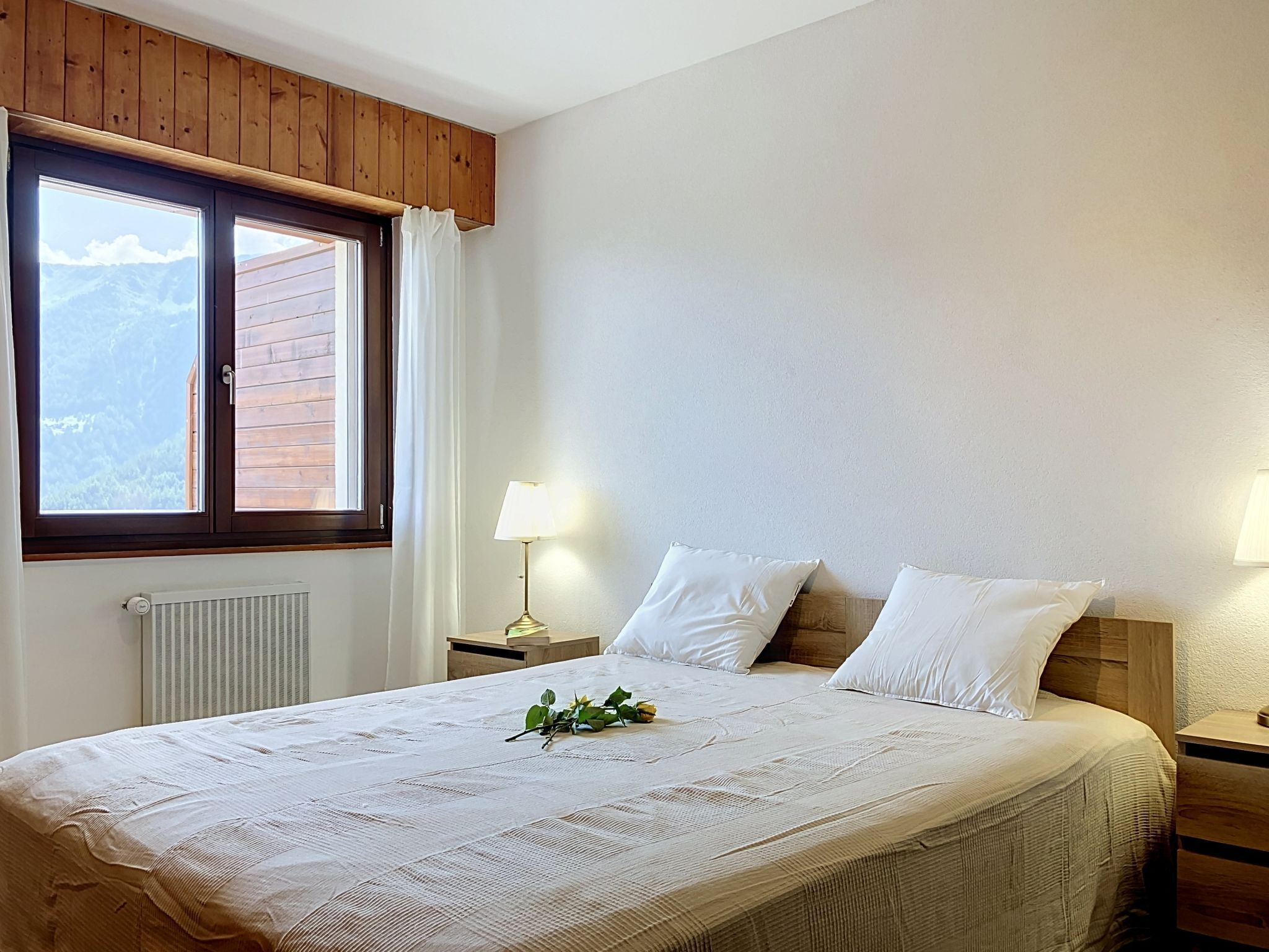 Une chambre avec un grand lit, une fenêtre avec des rideaux, une lampe de chevet et un radiateur.