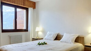 Quarto com uma cama grande, janela com cortinas, abajur e radiador.
