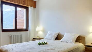 Une chambre avec un grand lit, une fenêtre avec des rideaux, une lampe de chevet et un radiateur.