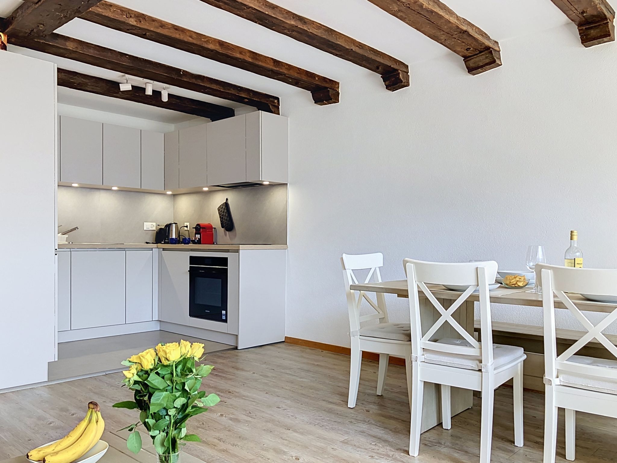 Une cuisine moderne avec des meubles blancs, une table à manger avec des chaises blanches et un plafond en bois.