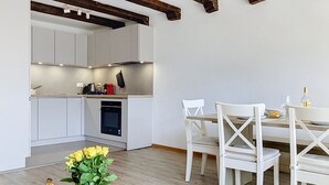 Uma cozinha moderna com armários brancos, uma mesa de jantar com cadeiras brancas e teto de madeira.