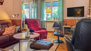 Uma sala de estar com sofá de couro, poltrona vermelha, cadeira de escritório preta, uma mesinha e uma televisão.