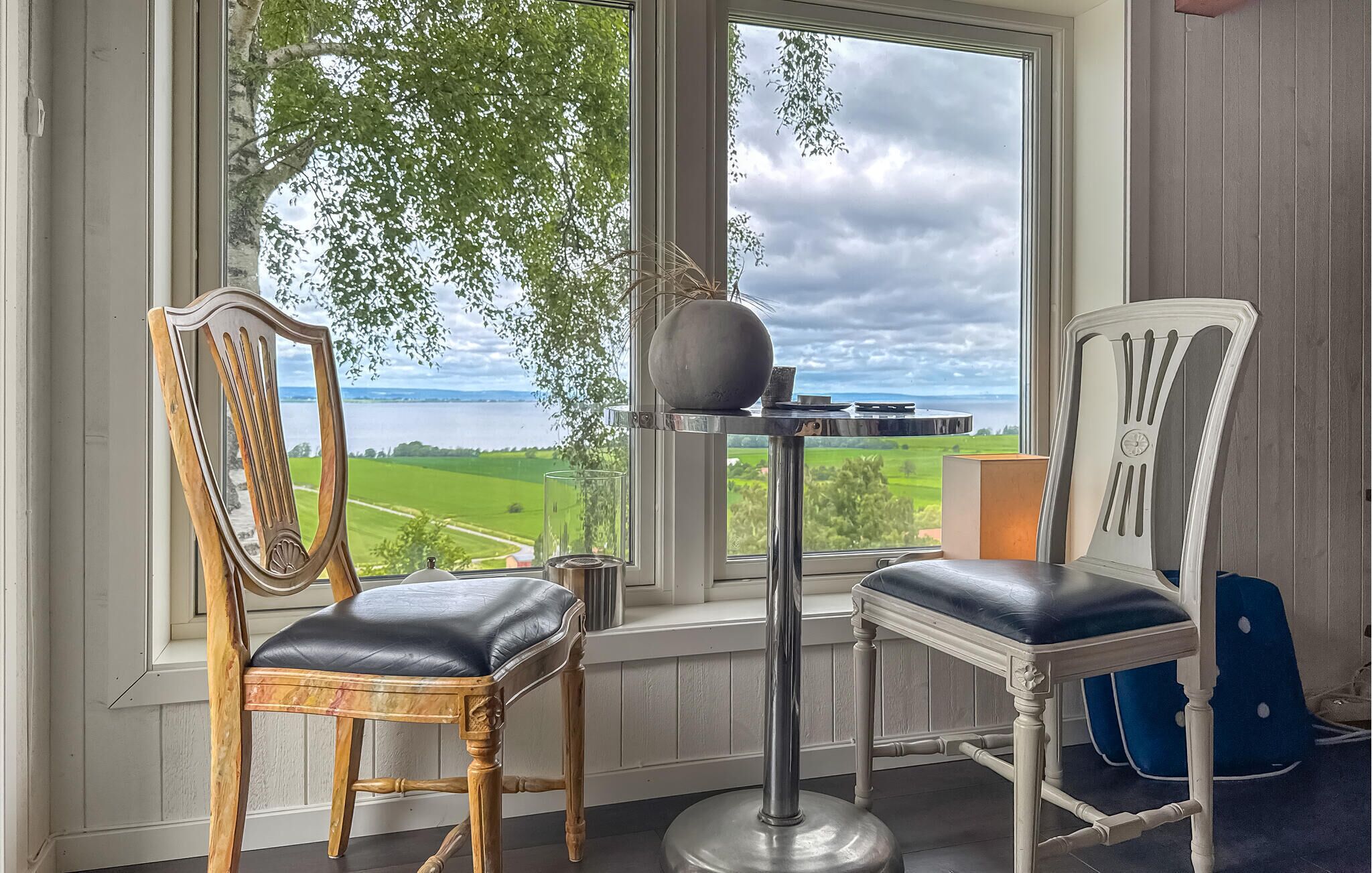 A room with two chairs, a table, and a view of a lake through a window.