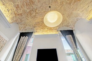 A room with a brick ceiling, a flat-screen TV, and a large window with curtains.