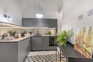 Eine moderne Küche mit grauen Schränken, einem eingebauten Backofen und einem Spülbecken. Auf der Arbeitsplatte stehen Pflanzen und an der Wand hängt ein Gemälde.