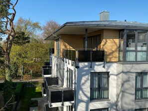 Ein modernes, mehrgeschossiges Gebäude mit Balkon, großen Fenstern und einer flachen Dachfläche.