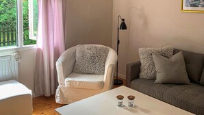 Ett vardagsrum med en vit fåtölj, en grå soffa, ett vitt soffbord med två glasburkar, en golvlampa och ett fönster med gardiner.