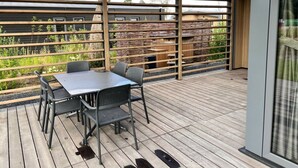 A covered outdoor patio with a table and chairs, a wooden fence, and a view of a garden. - Cube Split Hottub 6 (Enkhuizen)