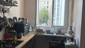 Een kleine keuken met een raam, een fornuis en diverse keukengerei.
