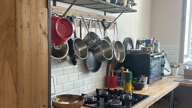 Een keuken met een houten aanrecht, een fornuis, en diverse pannen die aan de muur hangen.