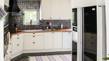 A compact kitchen with white cabinets, a black range hood, a window with a plant, and a striped rug.