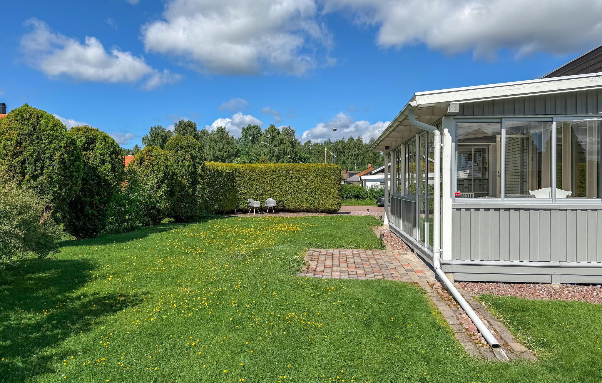 Ett hus med en inglasad veranda, en välklippt gräsmatta och en häck.