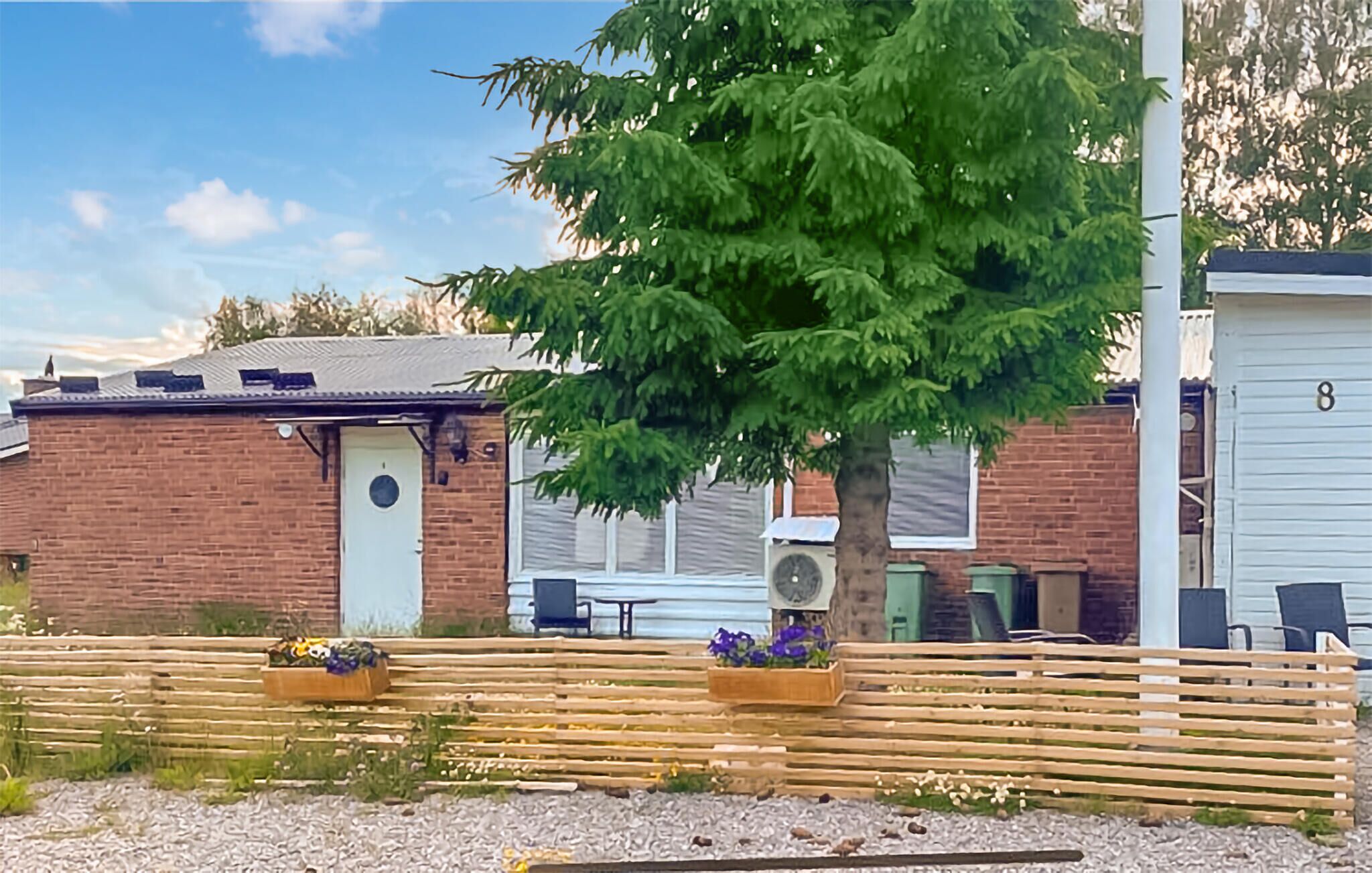A brick building with a white door, a large tree in front, and a wooden fence.